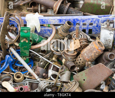 A close up of an assorted and jumbled collection of tools, engine and machine parts in a dirty blue plastic crate. On sale at a country show. Stock Photo