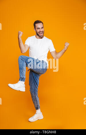 Full length image of ecstatic guy 30s in t-shirt and jeans laughing and rejoicing while standing isolated over yellow background Stock Photo