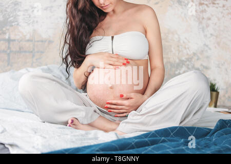 Crop photo of  beautiful pregnant girl young woman with long curly hair sitting in lotus pose on bed. Pregnancy yoga and nature ethnic beauty concept