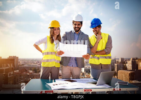 Architects team and engineers looking paper plans at construction site. Stock Photo