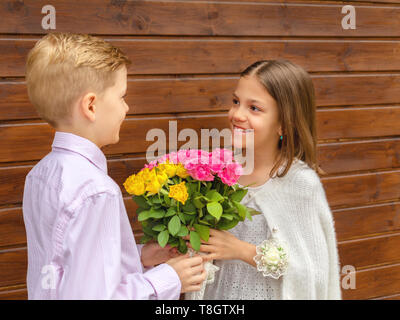 Cute little boy giving bouquet of flowers to charming little lady – smiling girl in love receiving yellow and pink roses from friend – generation z Stock Photo