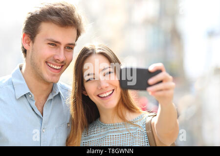 Happy couple taking selfies using smat phone in the street a sunny day Stock Photo