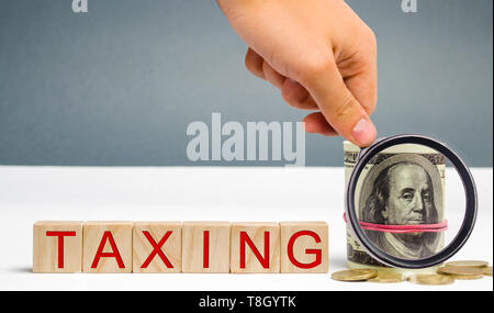 Wooden blocks with the word Taxing and dollars. Taxation, imposition of compulsory levies on individuals or entities by governments. Taxes on income,  Stock Photo