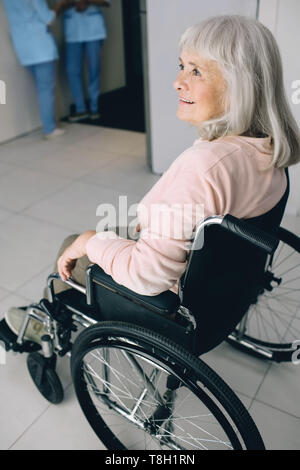 Smiling senior woman in wheelchair sitting at the hospital corridor. Go home after discharge from hospital Stock Photo