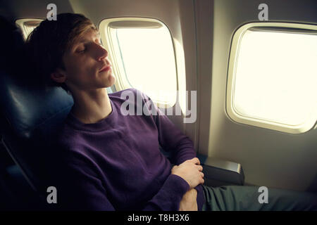 young man sleeping in an airplane seat. traveler in an plane Stock Photo