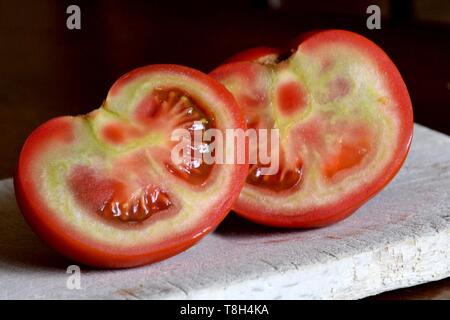 red raw tomato cut in half with green parts inside,immature tomato isolated,on wooden plate,red outside and green inside,healthy eating concept Stock Photo