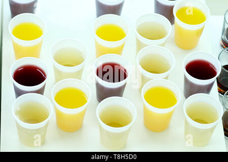 many plastic cups with various juice on white table served as a welcome drink on a party, event, wedding reception or banquet. Stock Photo