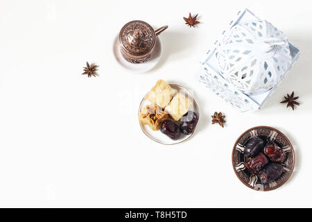 Ramadan Kareem greeting card, invitation. White lantern, bronze plate with dates fruit, baklava pastry, coffee cup on table. Iftar dinner. Eid ul Adha Stock Photo