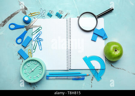 Open notebook with school stationery and alarm clock on light background Stock Photo