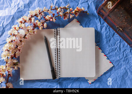 Opened notebook, pen and envelope in a frame of cherry blossoms on a bright background. Romance, love letters concept Stock Photo