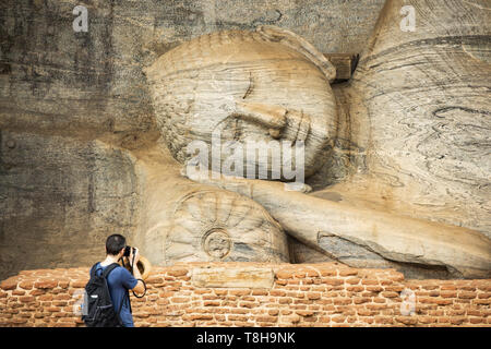 (Selective focus) A tourist is taking photos at the beautiful statue of the Reclining Buddha carved in stone. Stock Photo