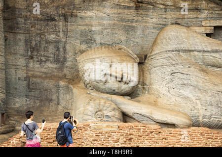 (Selective focus) A couple of tourists are taking photos at the beautiful statue of the Reclining Buddha carved in stone. Stock Photo