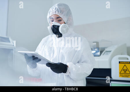 Biologist in protective costume using tablet Stock Photo