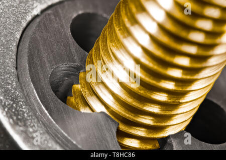 Steel threading die. Bronze bolt shaft in detail. Close-up of work with sharp cutting tool. Shiny brass threaded screw in gold color. Chip machining. Stock Photo