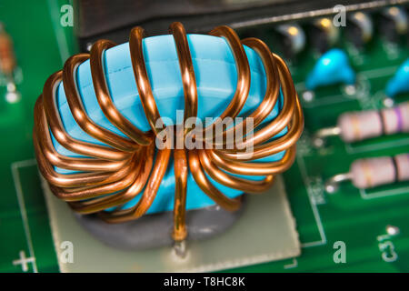 Copper wire winding. Inverter inductor detail. Colored electronic part. Beautiful blue coil in open electric power supply unit. Magnetic ferrite core. Stock Photo