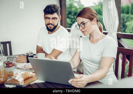Focused female working on laptop during breakfast with husband outdoors. Stock Photo