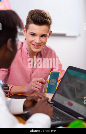 Teenager holding smartphone talking to African-American friend Stock Photo