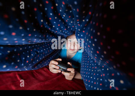 Boy, 8 years, sectretly playing a computer game in bed Stock Photo