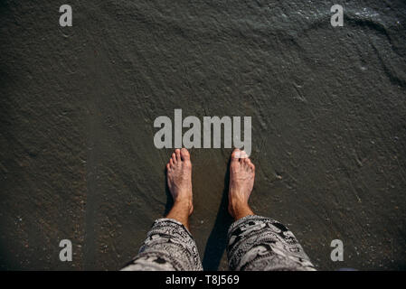 Man's feet standing on beach, Ban Ao Nang, Krabi, Thailand Stock Photo