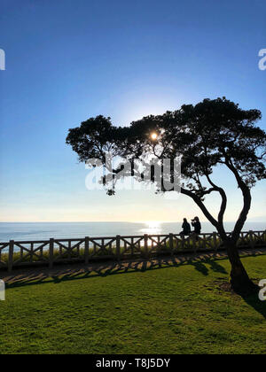Couple sitting on a fence taking photos and looking at the view, Santa Monica, California, United States Stock Photo