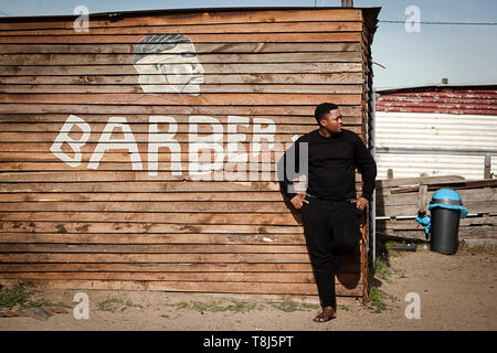 Amos Mgodini standing in front of his barber shop called Ayas in Wallacedene, Cape Town, South Africa. Stock Photo