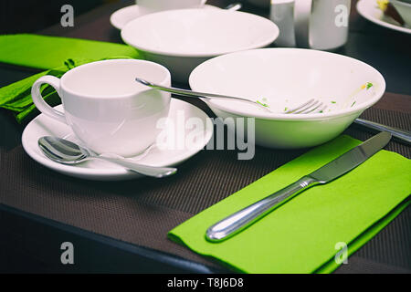 Used cutlery on the table. Coffee cup, plate, knife and spoons on the table. Selective focus Stock Photo