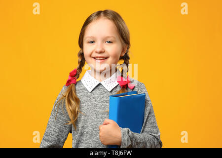 Closeup little girl schoolgirl on yellow background. The child is holding a book. The concept of education. Back to school. Stock Photo