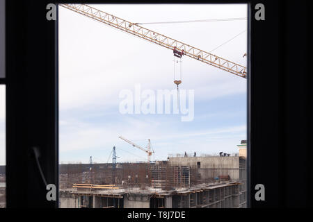 High-rise mighty hoisting crane and large building construction site with cranes with long yellow arrow against blue sky over new multi-storey concret Stock Photo