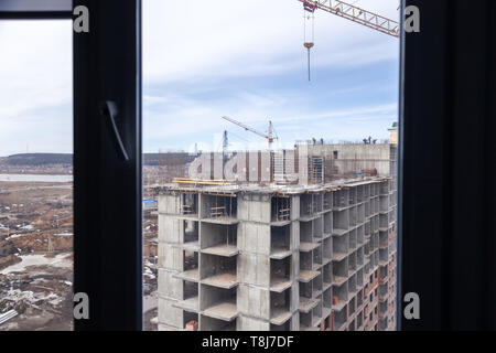 High-rise mighty hoisting crane and large building construction site with cranes with long yellow arrow against blue sky over new multi-storey concret Stock Photo