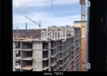High-rise mighty hoisting crane and large building construction site with cranes with long yellow arrow against blue sky over new multi-storey concret Stock Photo