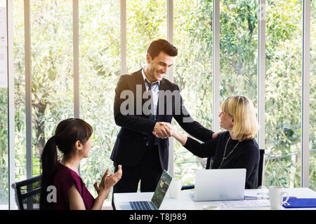 Business man and business woman shaking hands on meeting while female colleagues applauding in office Stock Photo