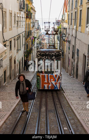 Lady walks on the tramlines in front of the Ascensor Da Bica, Lisbon's oldest funicular, Misericórdia, Lisbon, Portugal Stock Photo