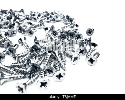 Small nickel-plated screws on a white background are scattered about randomly. Furniture fittings for installation. Stock Photo