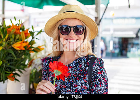 Young blonde mediterranean woman toothy smile in hat holding gerbera Stock Photo