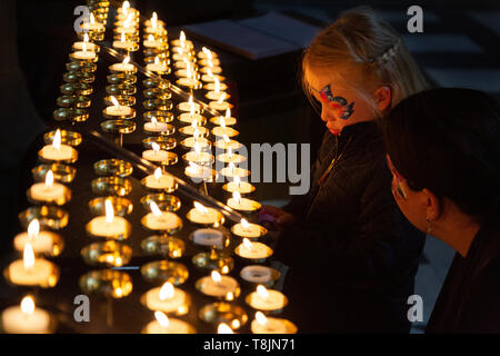 Child lighting a candle in church - a young girl with face paint being helped by her mother to light a candle; Worcester Cathedral, Worcester UK Stock Photo