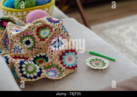 Multicolored plaid squares of crocheted on a cream colored seat background. In a basket with  of yarn, colors are green, pink, blue and  turquoise Stock Photo
