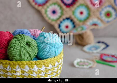 Multi Colored baby blanket and colorful yarns on sofa. Green, pink,cream, blue,red color yarns, scissors are  on the sofa. Stock Photo