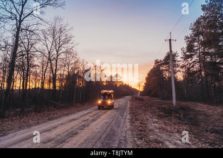 SUV rides on a dirt road, evening Stock Photo