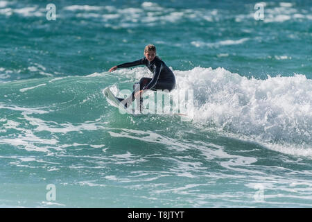 Surfing action as a young teenage female surfer rides a wave at Fistral in Newquay in Cornwall. Stock Photo