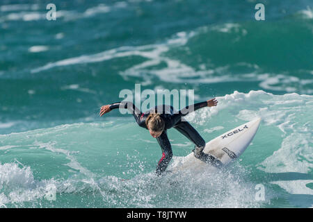 Surfing action as a young teenage female surfer rides a wave at Fistral in Newquay in Cornwall. Stock Photo