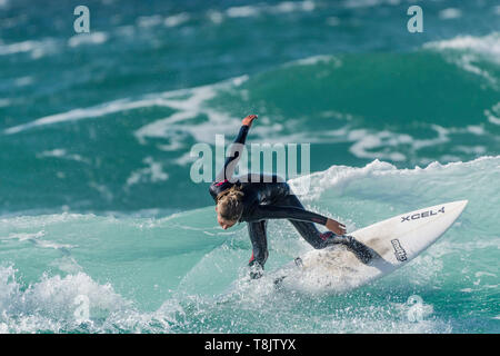 Surfing action as a young teenage female surfer rides a wave at Fistral in Newquay in Cornwall. Stock Photo