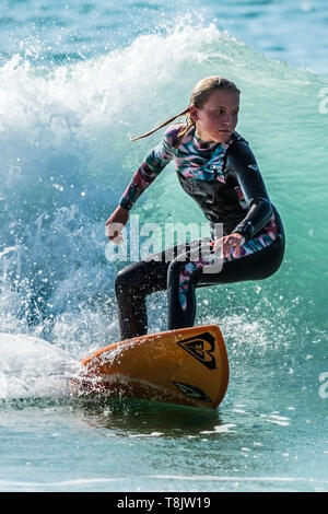 Surfing action as a young teenage female surfer rides a wave at Fistral in Newquay in Cornwall. Stock Photo