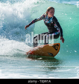 Surfing action as a young teenage female surfer rides a wave at Fistral in Newquay in Cornwall. Stock Photo