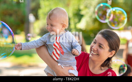 Cute baby and his mother catching soap bubbles in a summer day Stock Photo