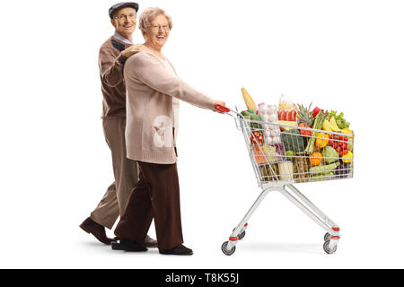 Full length shot of an elderly couple walking and pushing a shopping cart with food products isolated on white background Stock Photo
