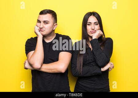 Photo of resented man and woman in casual clothes standing together and touching chin with irritated look isolated over yellow background Stock Photo