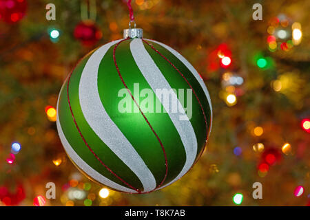large green and white and red christmas tree ornament with defocussed tree and lights behind it Stock Photo