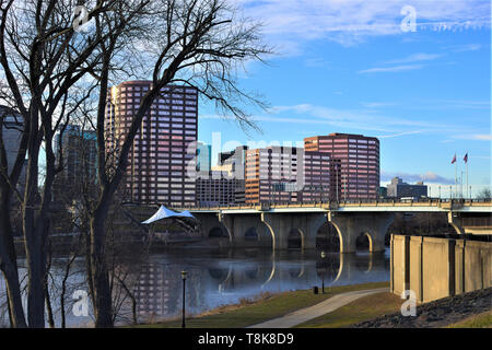 City buildings across the river with reflection in the water on a sunny day with blue sky and clouds Stock Photo