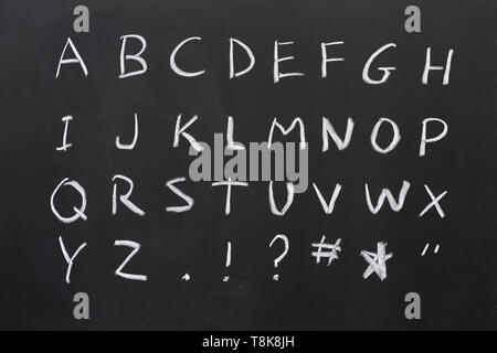 capital alphabet written in white chalk on a blackboard with some symbols Stock Photo