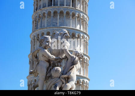 Sculpture of cupids holding a shield in front of the leaning tower of Pisa. The summer sky behind is clear and blue. Stock Photo